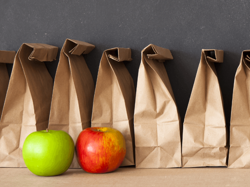 A row of brown paper bag lunches with apples