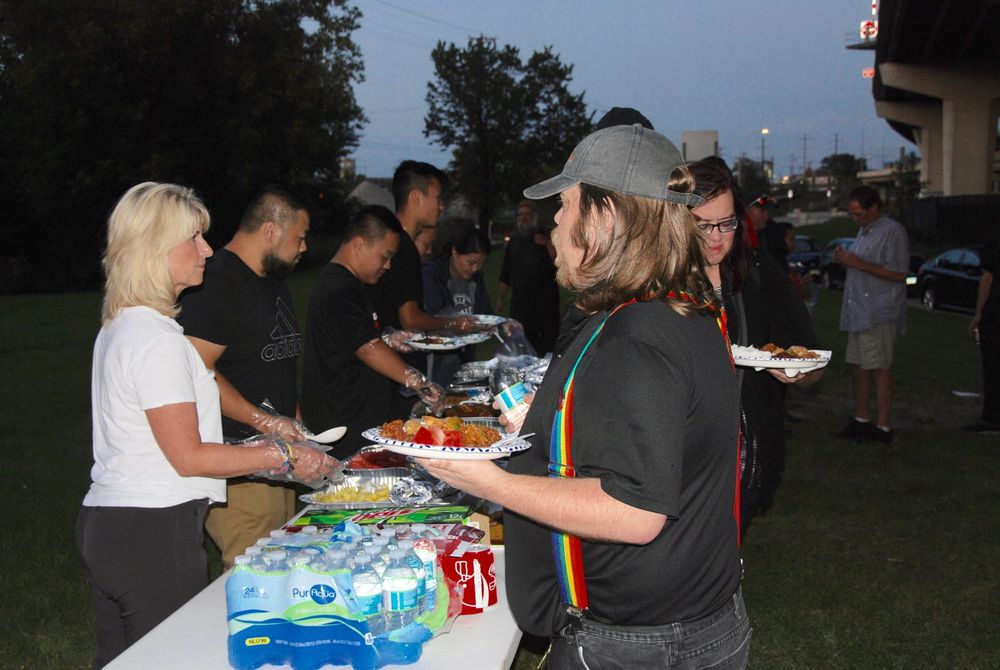 A line of people being served a hot meal at dusk